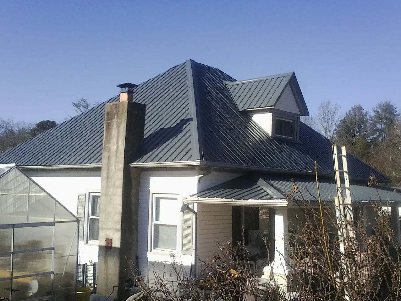 Dark blue standing seam metal roof on a white farmhouse with dormer — Slate & Tile Roof Repair by Roofing Brothers in Grinnell