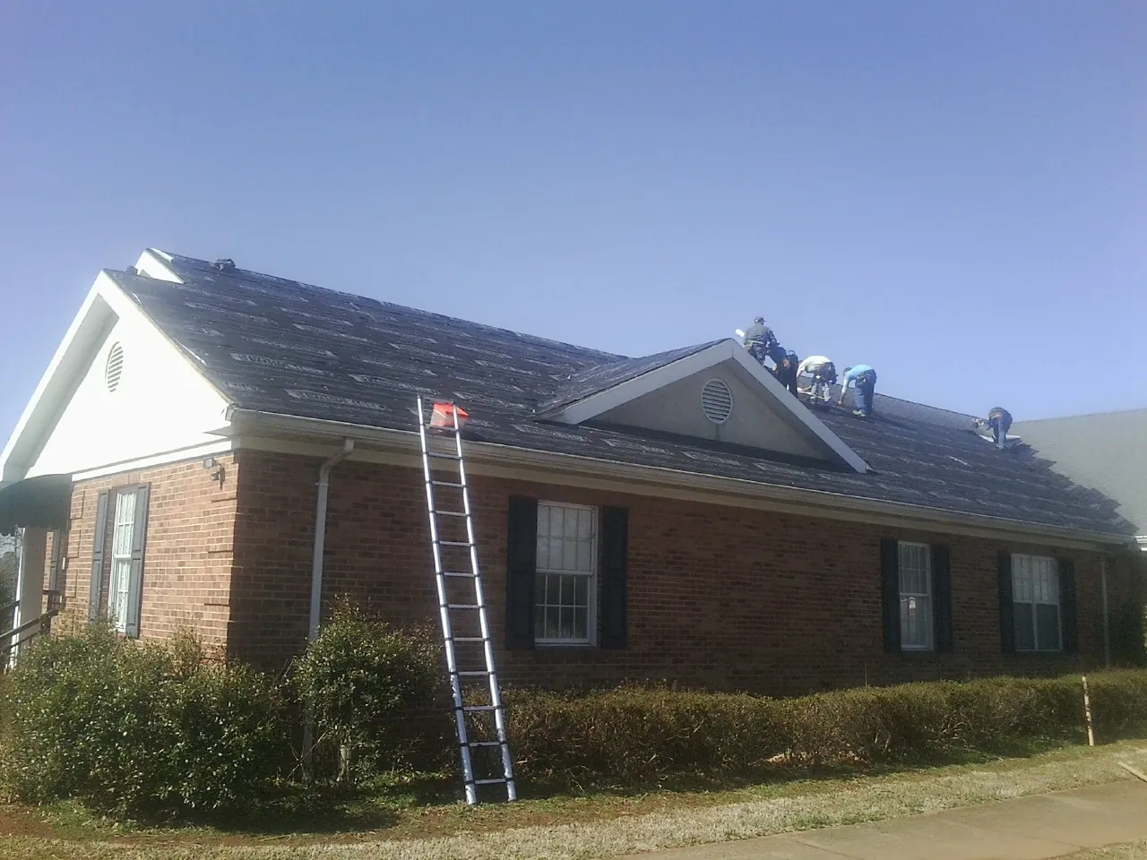 Crew tearing shingles off a brick ranch roof with a ladder set — Emergency Roof Repair work by our crew in Grinnell