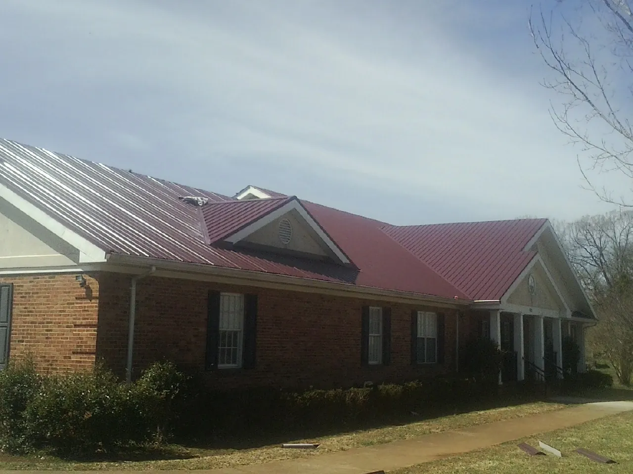 Red metal roof with gabled entries on a long brick building, from a Hail Damage Roof Repair job in Grinnell