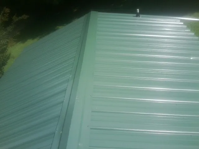 New green metal panels meeting at the ridge of a roof — Flat Roof Repair work by our crew in Grinnell