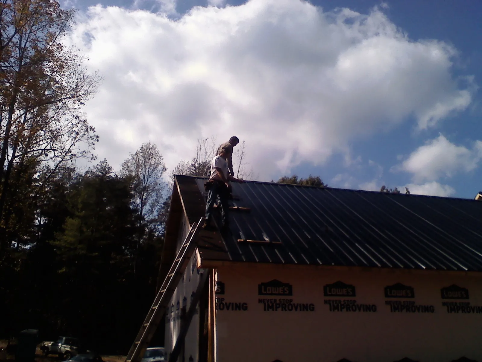 Roofer fastening dark metal panels high against a cloudy sky, from a Roof Inspection job in Grinnell