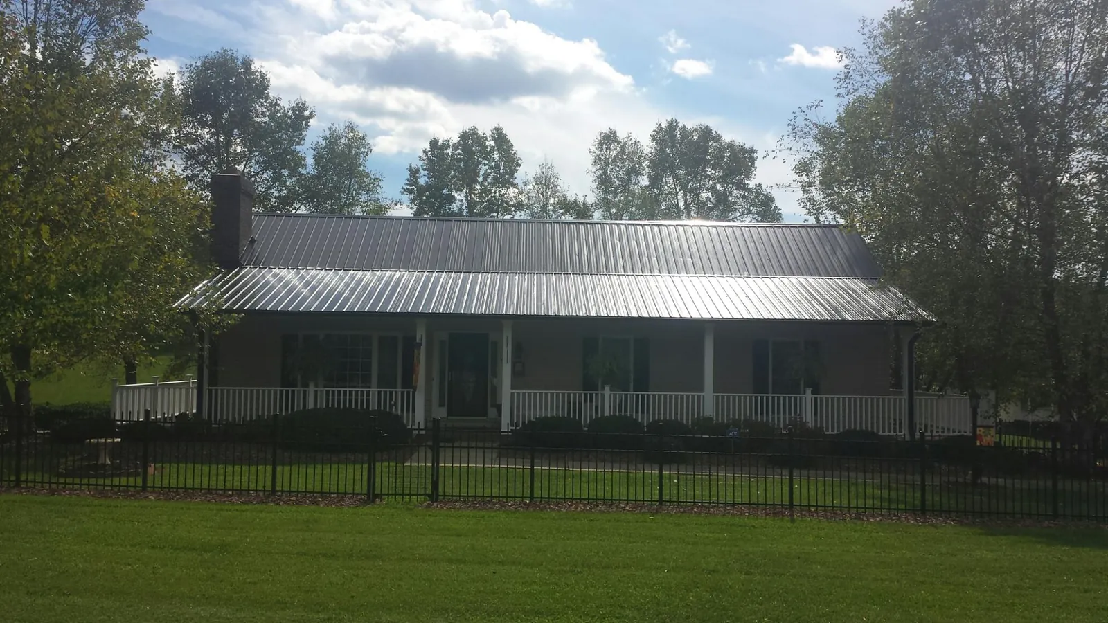 Gray metal roof on a brick ranch with a full width front porch — Gutter Guard Installation work by our crew in Grinnell