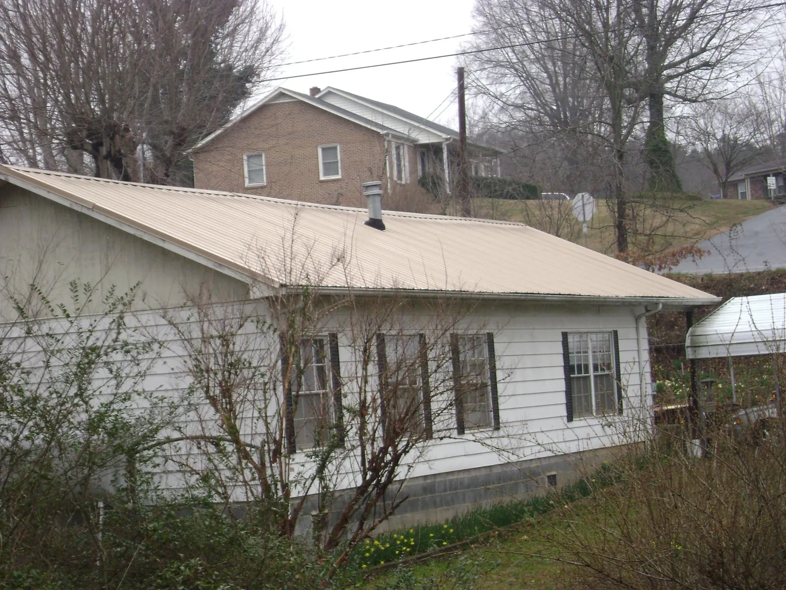 Tan metal roof on a white sided house set into a hillside — Commercial Roofing by Roofing Brothers in Grinnell