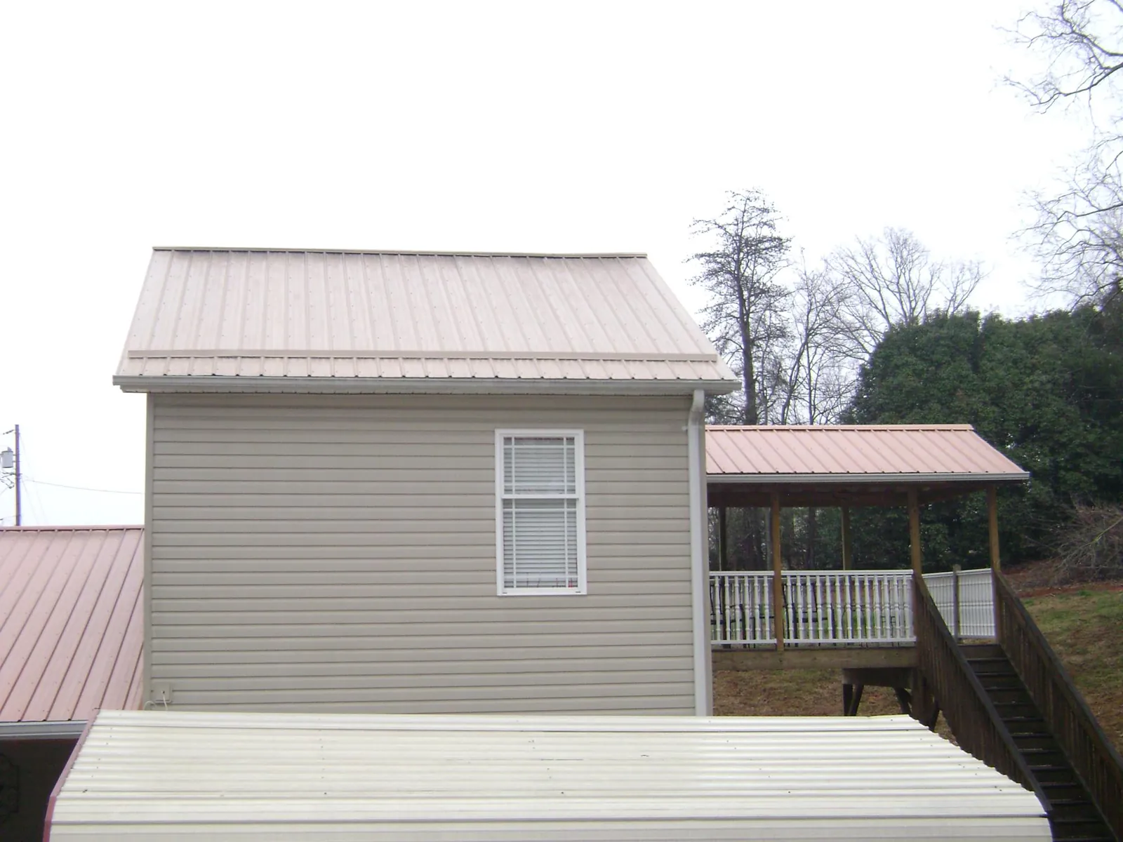 Tan metal roofs on a two story addition and attached porch, from a Roof Replacement job in Grinnell
