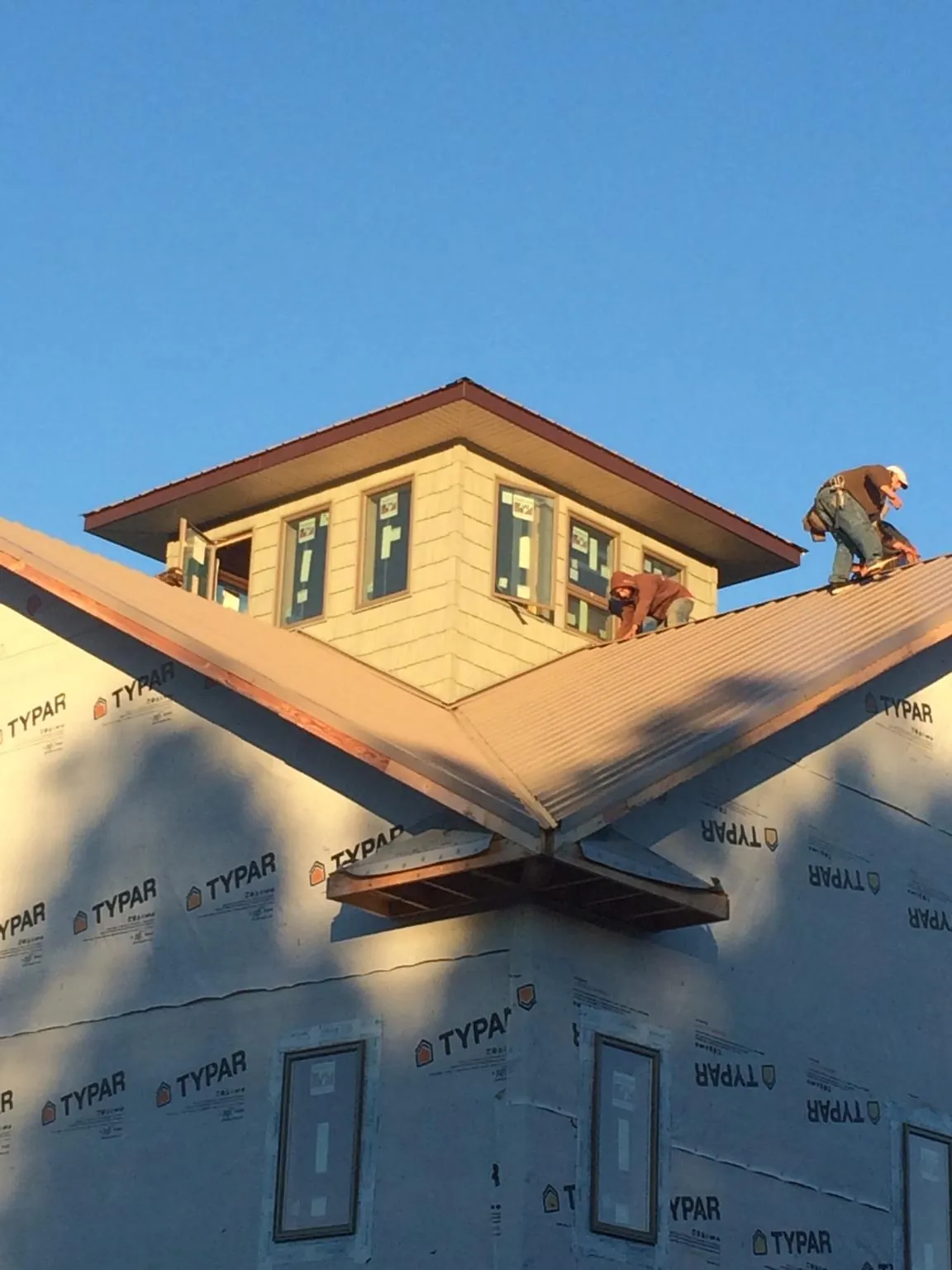 Roofers working around a rooftop cupola on a new metal roof at sunset — Roof Waterproofing in Grinnell by Roofing Brothers
